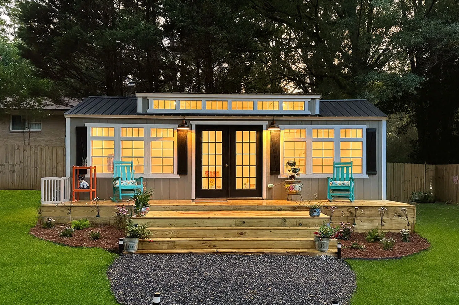 Tiny home with a dormer, French doors and a front deck, lit up at dusk